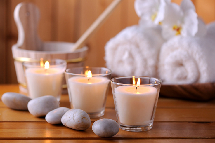 A row of three lit candles and smooth stones sit on a wooden bench in a sauna